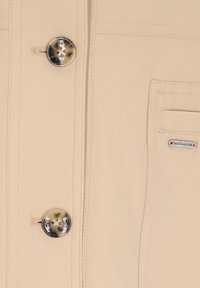 Beige Oberbekleidung mit glatter Stoffstruktur, zwei großen Knöpfen mit marmoriertem Effekt und einem dezenten Logo-Tag auf der Brusttasche.