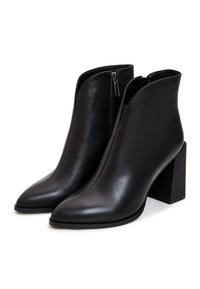 Bottines en cuir noir avec bouts pointus, talons carrés et fermetures éclair latérales internes, présentées côte à côte sur un fond blanc.