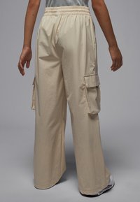 Beige cargo pants with an elastic waistband, loose fit, and side patch pockets. Smooth texture, mid-rise design, suitable for casual wear.