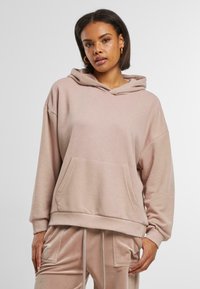 Lys rosa hettegenser laget av mykt stoff, med kengurulomme, oversized design og snorhette. Jevn tekstur.