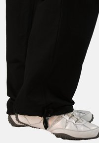 Black sweatpants with gathered cuffs and silver athletic shoes featuring a textured surface and black rubber soles.