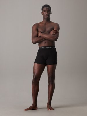 Zwarte katoenen boxershorts met een aansluitend ontwerp en een brede elastische tailleband met het "Calvin Klein" logo. Geshuwd door een staande mannelijke model.