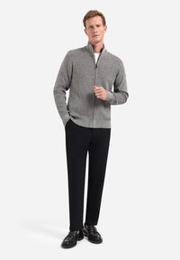 Grijze zip-up trui met een textuurpatroon, geribbelde manchetten en zoom, gecombineerd met zwarte broek en zwarte instappers. Eenvoudig, hedendaags ontwerp.