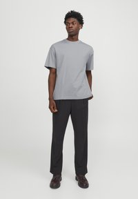 Light gray short-sleeve t-shirt with a crew neck, paired with dark trousers and brown lace-up shoes, standing on a plain background.