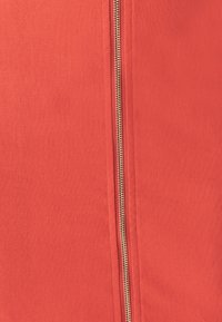 Rode stof met een gladde textuur heeft een centrale gouden rits. De rits strekt zich uit langs de lengte van het materiaal.