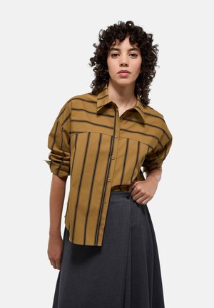 Chemise boutonnée jaune moutarde à rayures verticales noires, avec des manches retroussées et un col classique, associée à une jupe gris foncé.