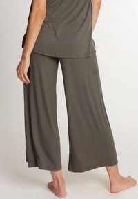 Brede, donkergrijze broek met een gladde textuur en een elastische tailleband, gecombineerd met een losvallende top. Zacht materiaal, casual ontwerp.