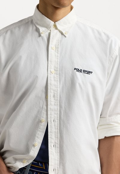 Cămașă albă cu nasturi, având un guler clasic, cu logo-ul „Polo Sport” de culoare bleumarin pe piept și fabricată dintr-un material neted.