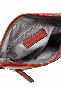Vnitřek červené kožené tašky s šedým podšívkou, obsahující kapsu na zip a koženou etiketu se značkou. Hladká textura a minimální vzor.