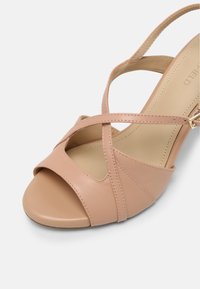 Nude-colored high-heeled sandal with crisscross straps made of smooth leather, peep-toe design, and a sleek ankle strap with gold hardware.