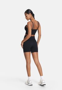 Crni atletski crops top i kratke hlače visokog struka od rastezljivog materijala. Ima tanke naramenice i bezšavni, glatki dizajn.