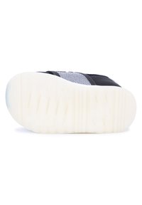 Black shoe with a textured upper, featuring white mesh accents. The sole is thick and rubberized, designed for grip with horizontal grooves.