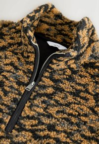 Fleeceový svetr se zipem, s texturovaným vzorem v hnědé, černé a šedé barvě, vysokým límcem a černými detaily.