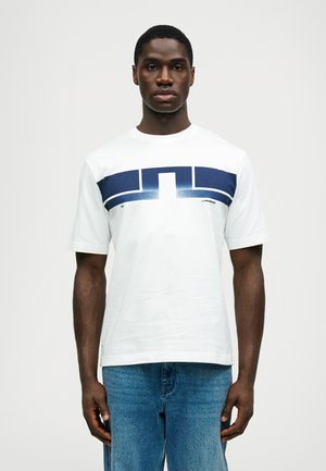 White cotton t-shirt with a navy blue graphic design across the chest, round neckline, and short sleeves. Worn with blue denim jeans.