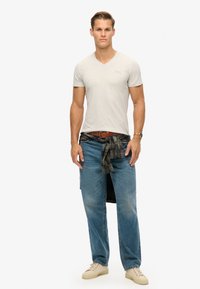 Grå V-hals t-shirt, blå jeans med lommer, og en flannel skjorte bundet om livet. Beigefarvede sneakers fuldender outfittet.