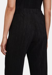 Černé plisované kalhoty s hladkou texturou, které mají elastický pás a vertikální pruhy po celé látce.