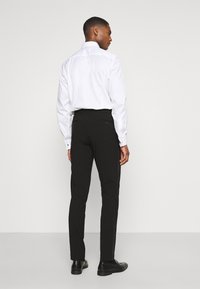 Cămașă albă cu guler ascuns, asociată cu pantaloni negri. Pantalonii au o croială slim și buzunare la spate, completându-se cu pantofi negri eleganți.