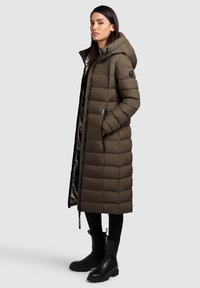Lang, olivengrøn pufferjakke med hætte og zip-lukning, der har quiltet polstring, sidelommer og et strømlinet design.