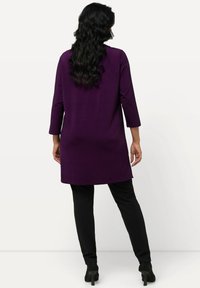 Tunika lunga viola con maniche a tre quarti e taglio dritto, abbinata a pantaloni neri. Tessuto morbido, design semplice, senza motivi visibili.