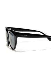 Black sunglasses with a glossy finish, featuring oversized round lenses and a thick, angular frame. Brand name "HAWKERS" is visible on the side.