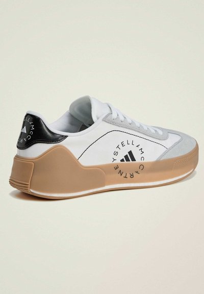 White sneaker with gray and black accents. Features a textured rubber sole and logo detailing on the heel and side. Smooth fabric upper.