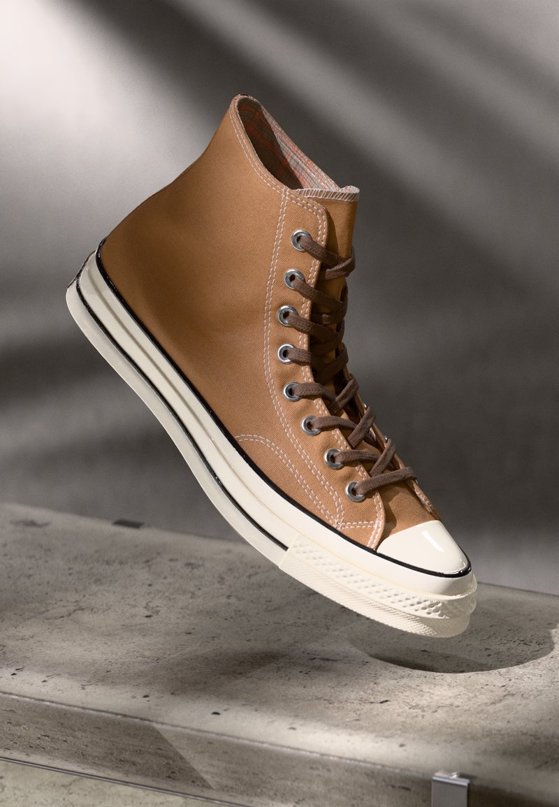 Brune høyhælte sneakers i kanvasmateriale, hvit gummisåle, metalløyler og brune snører. Har en teksturert overflate og et mønstret indre.