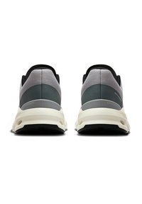 Pelēki un melni sporta apavi ar teksturētu sietu augšdaļu, noapaļotu papēdi un balto starpnesi, kas rotāti ar "SPEEDBOARD" detaļu uz sāna.