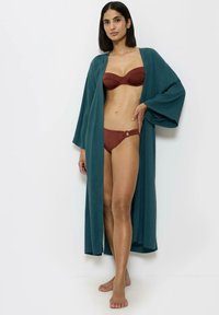 Turkusowy kimono z szerokimi rękawami nałożone na brązowy biustonosz na drutach i dopasowane majtki. Gładki materiał o luźnym kroju z detalem w postaci guzika.