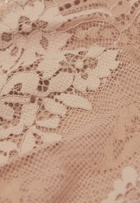 Nude koronkowy materiał z misternymi wzorami kwiatowymi i miękką, teksturowaną powierzchnią, z drobnymi detalami i delikatnym, warstwowym wyglądem.