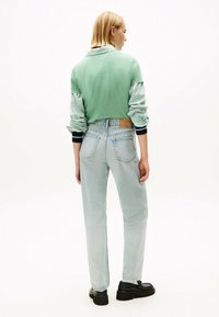 Sudadera recortada verde claro con mangas a rayas, combinada con jeans rectos azul claro y zapatos de plataforma negros. Detalles mínimos.
