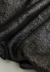 Czarna tkanina o błyszczącej, teksturowanej powierzchni z metalicznym połyskiem i małymi refleksyjnymi cząsteczkami, złożona w warstwowe draperie.