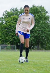 Nike treniruočių apranga šviesiai rožinės spalvos su mėlynais akcentais, derinama su mėlynomis šortais ir juodomis kojinėmis. Futbolo kamuolys ilsisi ant žolės.
