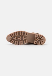 Suola di scarpe in gomma marrone con una presa testurizzata e a motivo. Presenta numerose scanalature triangolari e rettangolari per la trazione.