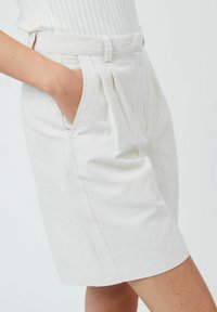 Helle beigefarbene Tailored-Shorts aus einem strukturierten Stoff, mit seitlichen Taschen und subtilen Fältchen an der Taille.