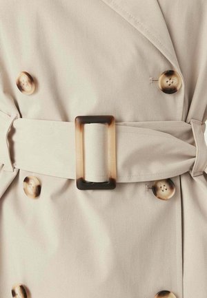 Lichtbeige trenchcoat met grote schildpadknopen en een bijpassende stoffen riem met een rechthoekige schildpaddensluiting.