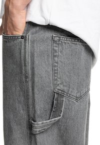 Grå denimbukser med en sidelomme og synlige sømdetaljer. Stoffet har en blød tekstur og er designet til en afslappet pasform.