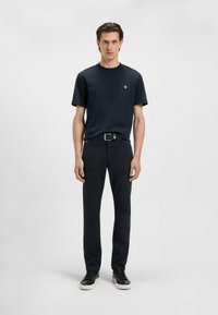 Mörkblå t-shirt med rund hals och en liten emblem, kombinerad med mörka byxor och svarta sneakers, med en mjuk textur och smal passform.