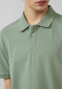 Polo en algodón verde apagado, con cuello con solapa, tres botones a juego y mangas cortas de textura suave.