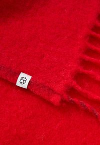 Red wool scarf with a soft texture, featuring fringe edges and a small white label. The fabric appears cozy and warm.