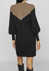 Robe en tricot avec un design en blocs de couleurs brun et noir, avec un détail en forme de V au dos et des manches bouffantes.