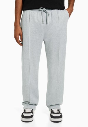 Lichtgrijze joggingbroek met elastische tailleband en trekkoord. Beschikt over twee zijnaden en een relaxte pasvorm. Gecombineerd met zwart-witte sneakers.