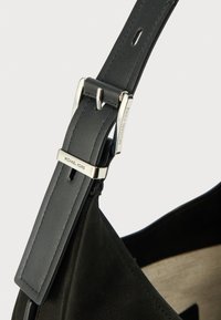 Sac à main en cuir noir avec bandoulière et boucle en métal argenté. Présente une texture lisse et un logo "Michael Kors" bien visible.