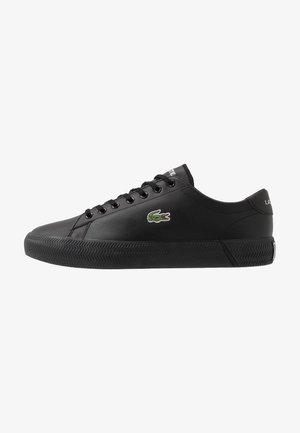 Czarny niskoprofilowy sneaker z czarnymi sznurowadłami, teksturowaną podeszwą i małym zielonym logo krokodyla z boku.