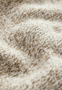 Tissu doux et texturé avec un motif tricoté en laine beige et crème montrant des boucles et une surface légèrement surélevée.