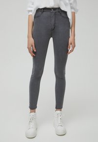Jean skinny gris en denim, présentant un design traditionnel à cinq poches, une taille haute et une texture lisse, assorti à des baskets montantes blanches.