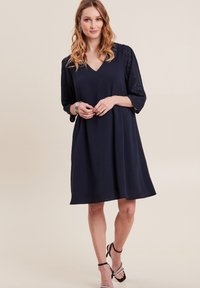 Marineblaues Kleid mit V-Ausschnitt, dreiviertel-langen Spitzenärmeln und einer lockeren A-Linie. Sanfter Stoff mit subtiler Textur.