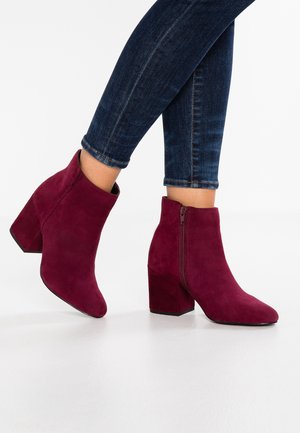 Kvinde iført mørkeblå skinny jeans og bordeaux ruskind ankelstøvler med blokhæl og sidelommer.