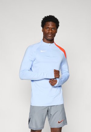Lange mouwen lichtblauw sporttop met een hoge kraag, oranje schouderpaneel en duimopeningen. Gepaard met grijze shorts met een zwart logo.