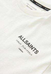 Bílý bavlněný tričko s kulatým výstřihem, černý potisk s nápisy "ALLSAINTS" a "LONDON", s jemnými japonskými znaky pod nimi.