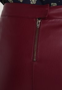 Burgundy kožená sukně s bočním zipem a stříbrným kovovým táhlem YKK. Hladká textura se strukturovaným designem a viditelnými švy.
